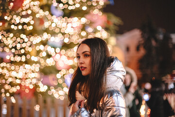 Portrait of pensive young woman standing by Christmas tree in city at night