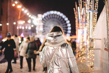 Fototapeta na wymiar Back view of young woman walking in Christmas market in city at night