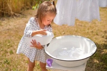 Cute beautiful little girl pours laundry detergent from a large white bottle. Safe bleaching of...
