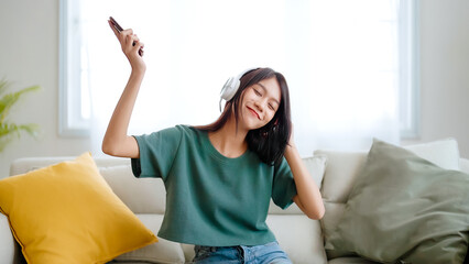 Young asian woman listening to music on couch in living room at home. Happy asia female using...