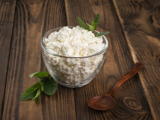 A dark wooden spoon next to a large bowl of fresh cottage cheese on a wooden table.