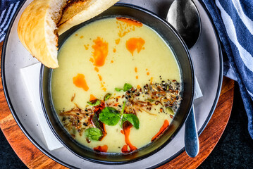 A serving of pumpkin soup in a round dark bowl, Spoon to the side and a piece of toasted bread