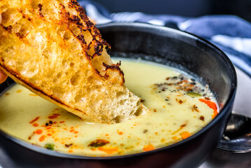 A piece of toasted bread being dipped into a serving of pumpkin soup in a round dark bowl