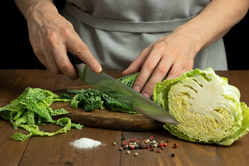 Female hands cutting Savoy cabbage on wooden table. Preparation of product for cooking.