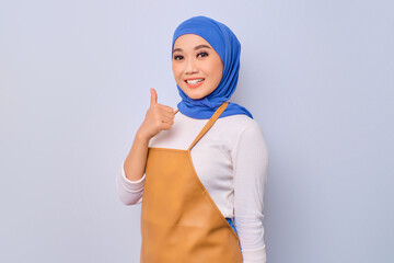 Smiling pretty young barista girl in apron showing thumb up gesture isolated on white background