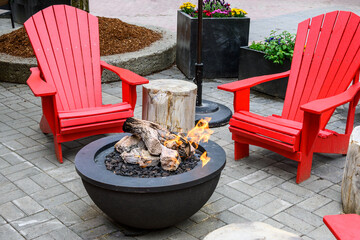 Bright red Adirondack chairs around a gas fire pit, seating in an outdoor gathering place
