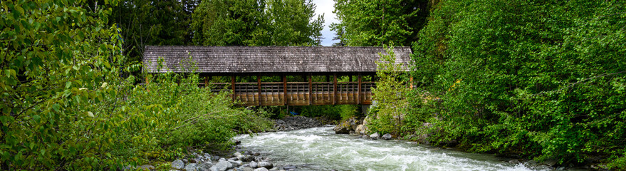 View of Fitzsimmons Creek and a covered wooden bridge over the whitewater river, Whistler, BC, Canada
