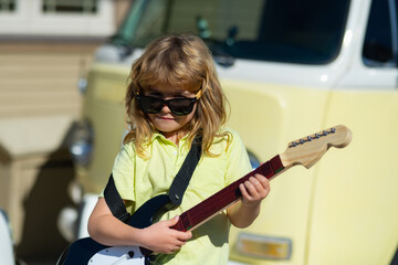 Funny rock child with guitar. Little boy in sunglasses. Kids music concept. Child musician playing...