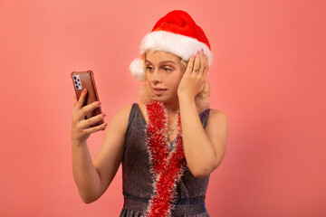 Surprised shocked young woman in Santa Claus hat, silver sparkly glitter dress with red tinsel...