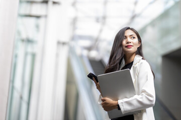 Portrait of a cheerful young Asia woman smiling while working on a laptop and smartphone in the office.