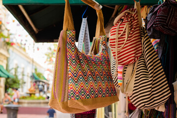 Backpacks, purses and handbags made with typical Mexican fabrics hanging outside souvenir stores.