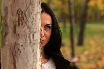 Brunette woman hiding behind the tree in autumn park
