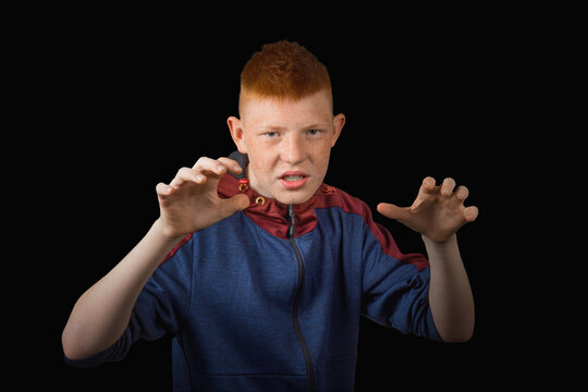 A teenager, a red-haired boy threateningly raised his hands up with an angry expression on his face, against a dark background.