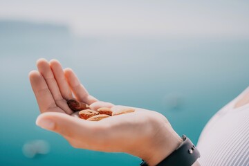 Young milky almond nuts in womans hand. A young caucasian woman eating fresh almond after morning fitness yoga near sea. Only hands are visibly. Healthy vegan food.