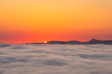 Fototapeta na wymiar 雲の彼方の山並みから昇る太陽