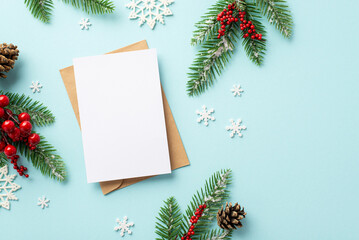 Fototapeta na wymiar Winter holidays concept. Top view photo of craft paper envelope postcard fir branches pine cones mistletoe berries and snowflakes on isolated pastel blue background with copyspace