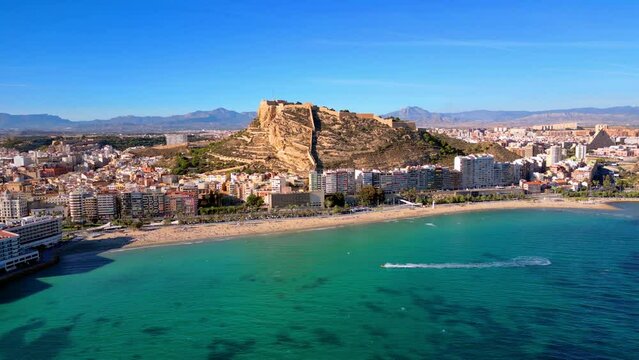 Playa de postiguet in Alicante Spain with the castillo de santa barbara in the background. Hotels and beach in the foreground. 4k aerial drone shot.