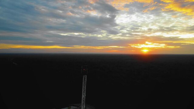Cinematic Drone Footage of Onshore Drilling Rig equipment structure for oil exploration and exploitation in the middle of jungle surrounded by palm oil trees during sunset and high oil price.
