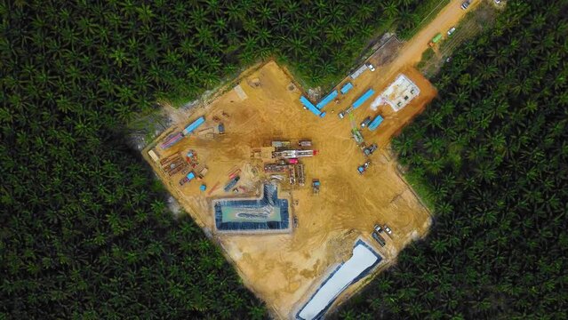 Cinematic Drone Footage of Onshore Drilling Rig equipment structure for oil exploration and exploitation in the middle of jungle surrounded by palm oil trees during sunset and high oil price.