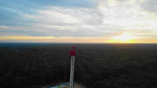 Cinematic Drone Footage of Onshore Drilling Rig equipment structure for oil exploration and exploitation in the middle of jungle surrounded by palm oil trees during sunset and high oil price.