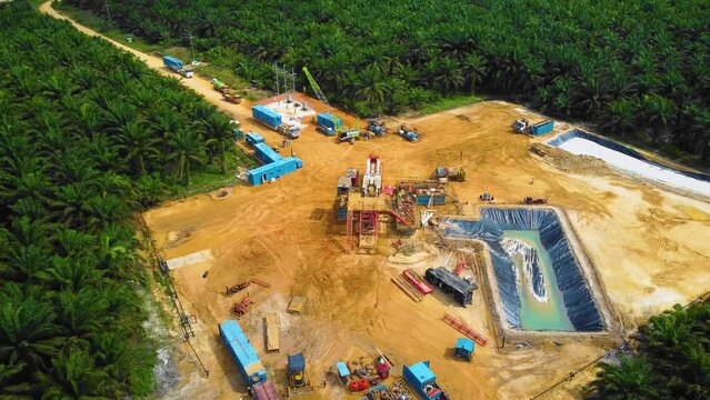 Cinematic Drone Footage of Onshore Drilling Rig equipment structure for oil exploration and exploitation in the middle of jungle surrounded by palm oil trees during sunset and high oil price.