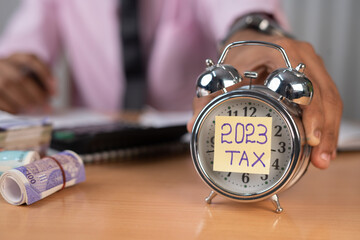 businessman placing timer with 2023 tax while calculating financial bills at office table - concept...
