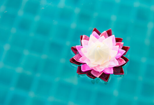 Handmade multicolour ribbon flower floating on blue water, craft idea lotus flower made from plastic ribbon