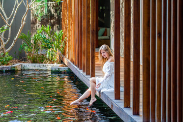 Woman on wooden bridge in Japanese garden feeding fish