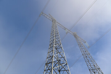 Pylon for high voltage transmission line in fog. View from the bottom of the tower of the cables and glass insulators.