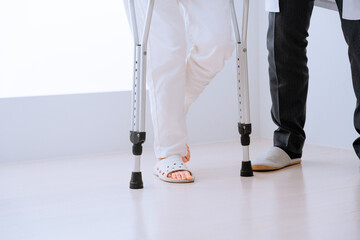 医者に介助されながら松葉杖をついて歩くミドル女性　リハビリイメージ - obrazy, fototapety, plakaty