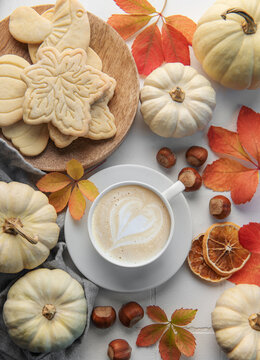 Hot coffee with cookies in a white cup  surrounded by autumn leaves and pumpkins on a white wooden background.