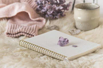 Cozy coffee break scene with notebook, cup and wool fabric, cream and lilac colors