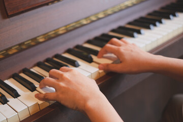 A close up of Hand playing a beautiful wood old-fashioned piano. Concept of practicing piano at home, Classical Musical instrument, The pranist learning and performing in studio. Hobbies and lifestyle