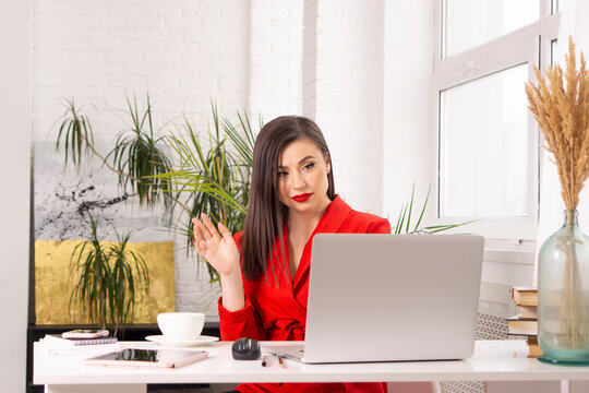 Young Elegant Brunette Businesswoman With Red Lips Waving At Laptop During Virtual Meeting In Office