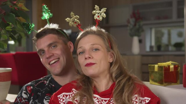 PORTRAIT: Joyful couple in festive mood singing and dancing on Christmas Eve. Cheerful twosome in Christmas sweaters celebrating holidays and enjoying relaxing festive time on comfortable sofa.