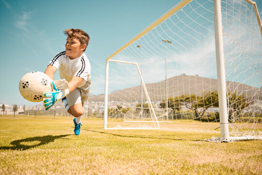 Football, boy goalkeeper and jump, saving ball from goals at outdoor sports field. Soccer, kid and competition game with fitness, goal keeper and soccer ball on grass, success and action to save goal