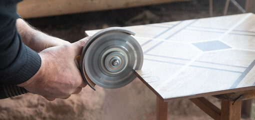 Worker cutting a ceramic tile with a grinder.