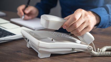 Businessman holding telephone receiver at the office table.
