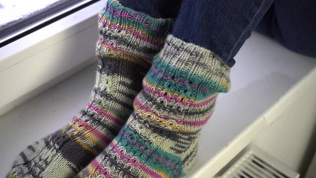  Girl legs in knitted striped socks near heating battery and window