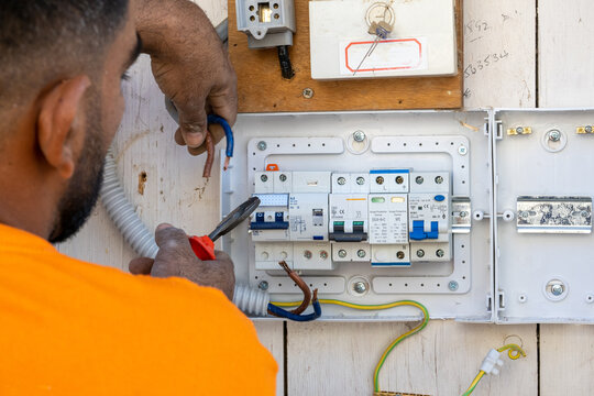 An Electrician At Work Repairs The Wiring In An Old House. The Master Changes The Electrical Panel. The Engineer Connects The Wires To The Fuses.