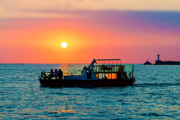 Silhouette of a boat and passengers of tourists in selective focus at sunset on the sea horizon in Sevastopol, Crimea on July 17, 2022. Сoncept of evening sea walks, vacation at sea.