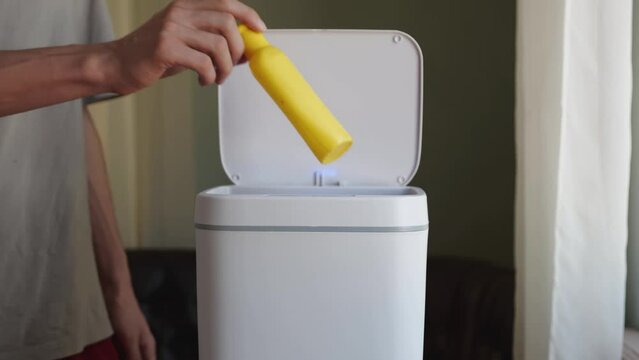 A man throws an empty plastic shampoo container into a household trash can. Plastic HDPE bottle waste