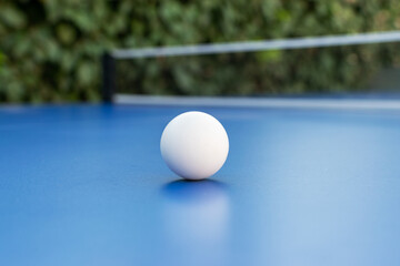 White ping pong ball on outdoor ping pong table with selective focus, unfocused background.