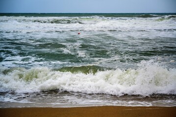 Big surf and wave in windy weather on sand beach.