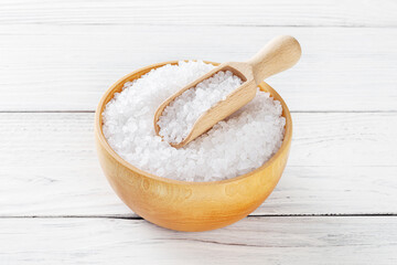 Sea salt in wooden bowl with scoop on white wooden background