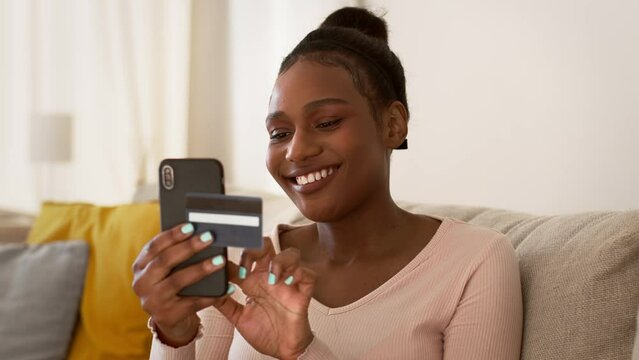 Mobile banking. Young african american woman making online transaction with credit card and smartphone, tracking shot
