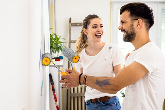 Smiling young couple painting wall in their home together.