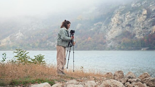Young caucasian woman professional photographer at work. A person standing next to a camera on a tripod and enjoying a beautiful view of the mountains.