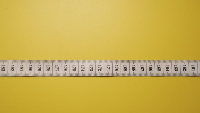 Centimeter tape or tailor's meter moving towards an increase in scale on a yellow background. Place for the inscription at the top. Concept of sewing skills. Stop motion animation