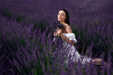 Beautiful young woman with bouquet sitting in lavender field